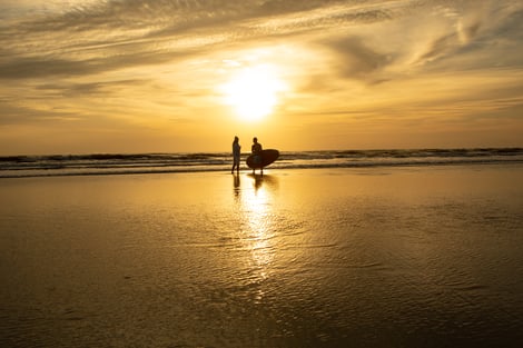 Two surfers walking the shoreline at sunset on New Smyrna Beach